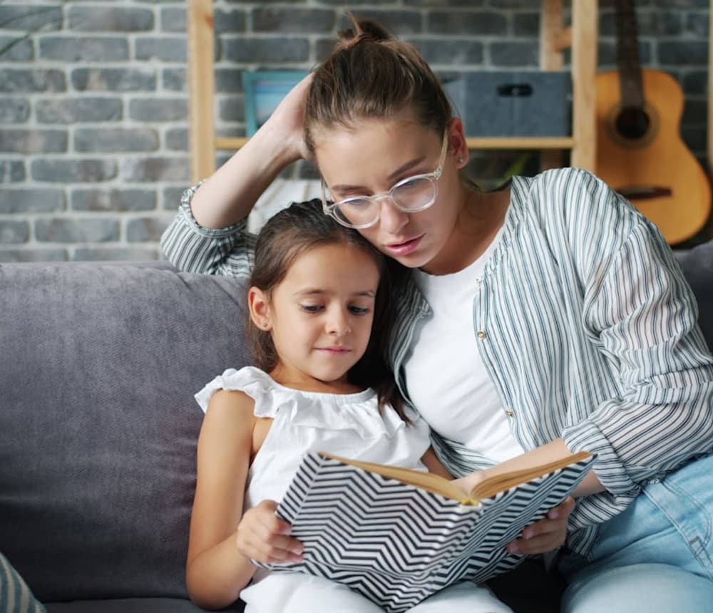 A caregiver reading a book with a child on the couch